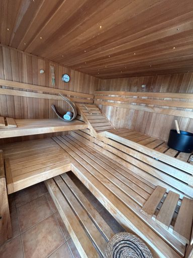 Saunainnenraum mit Holzverkleidung, Bänken und einem Eimer für Wasser.