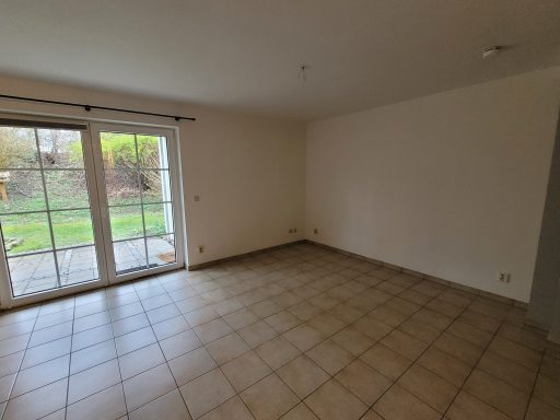 Leere, helle Wohnräume mit Fliesenboden und großen Fenstern zur Gartenseite.