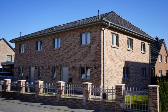 Zweifamilienhaus aus rotem Backstein mit grauem Dach und Gartenzaun.