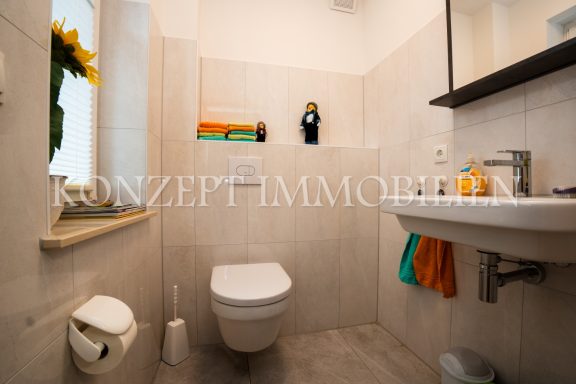 Kleine, moderne Toilette mit Waschbecken und Dekoration auf dem Regal.