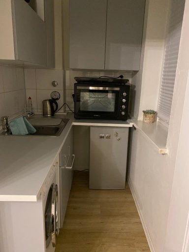 Kleine Küche mit einem Kühlschrank, Ofen und Spüle, hellgrauen Schränken und Holzfußboden.