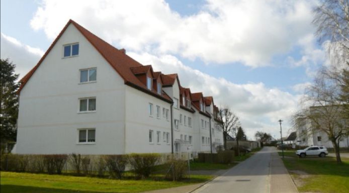Reihenhaus mit weißer Fassade und roten Dächern, umgeben von einer Straße und Bäumen.