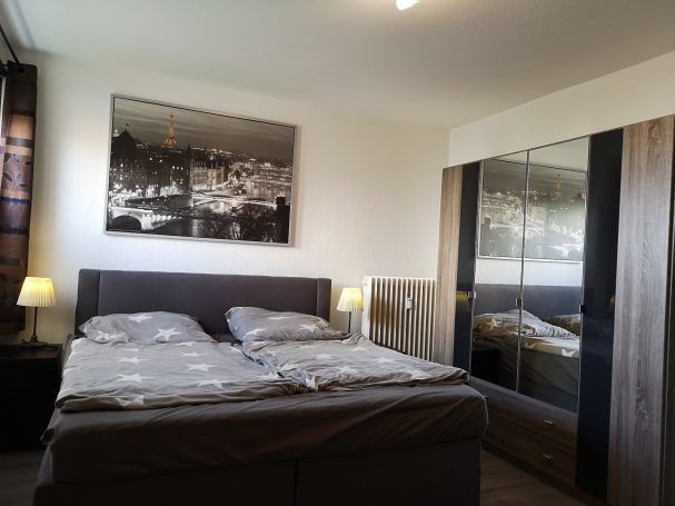 Helles Schlafzimmer mit Doppelbett, Spiegelkleiderschrank und zwei Nachttischlampen.
