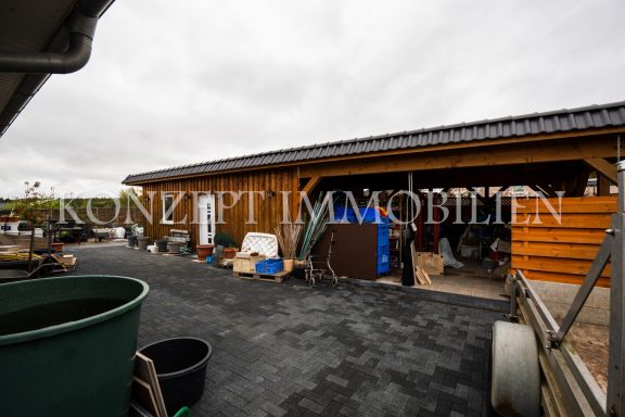 Holzgebäude mit Mülltonnen, Werkzeugen und verschiedenen Gegenständen im Außenbereich.