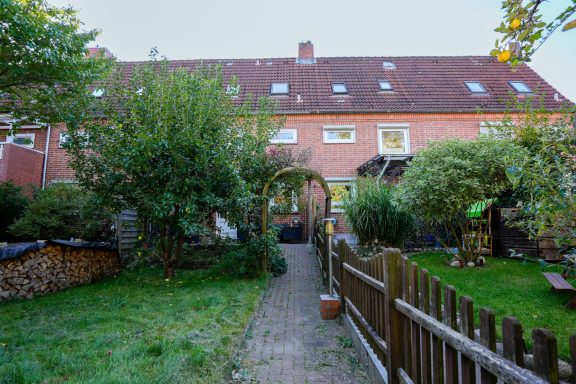 Hinterhof mit Garten, Wegen, Bäumen und einem Torbogen. Häuserzeile im Hintergrund.