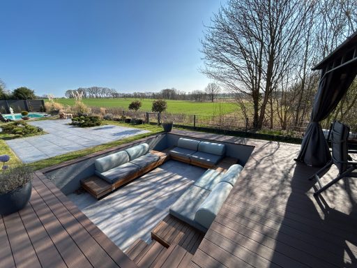 Gemütliche Außenlounge mit Sitzgelegenheiten, Blick auf grüne Wiese und Bäume.