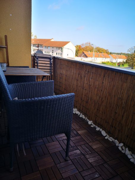Ein Balkon mit einem Tisch, zwei Stühlen und sichtbaren Gebäuden im Hintergrund.