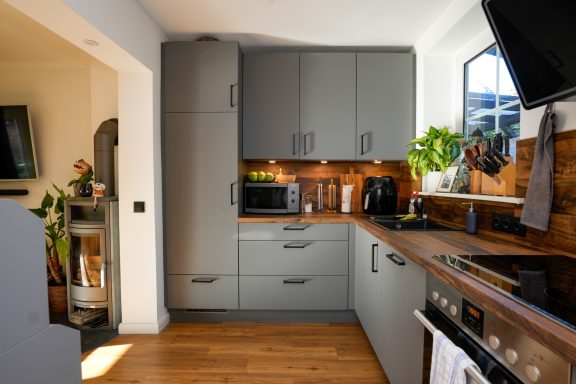 Moderne Küche mit grauen Schränken, Holzdetails und Geräten in warmem Licht.