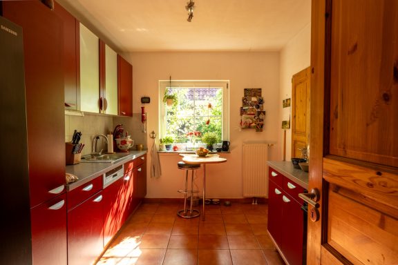 helle Küche mit roten Schränken, Esstisch vor Fenster und Pflanzen auf der Fensterbank
