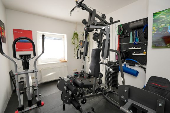 Heimfitnessstudio mit Trainingsgeräten und einem Fenster im Hintergrund.