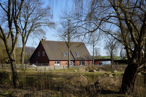 Rotes Haus mit Satteldach, umgeben von Bäumen und wilder Landschaft.
