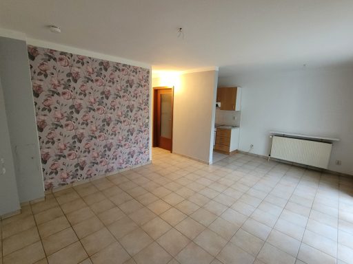 Heller Raum mit Fliesenboden und einer Wand mit Blumenmuster, heller Eingangstür.