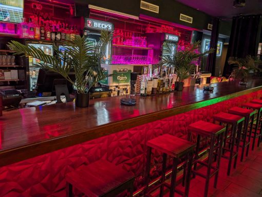 Moderne Bar mit leuchtend pinker Beleuchtung und stilvollen roten Hockern.