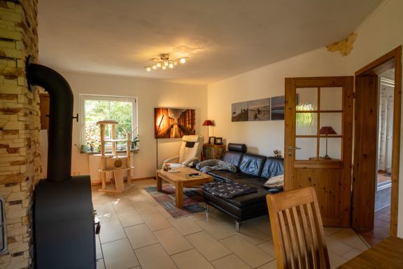Gemütliches Wohnzimmer mit Holzofen, Ledersofa, Esstisch und großem Fenster