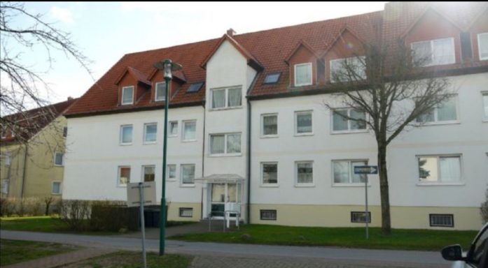 Mehrstöckiges Wohngebäude mit rotem Dach und naher Straße.