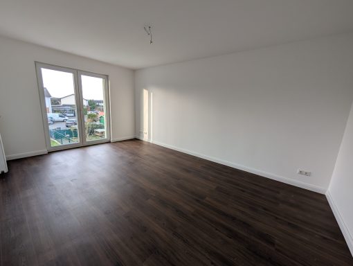 Helle, leere Wohnung mit dunklem Holzboden und großen Fenstern.