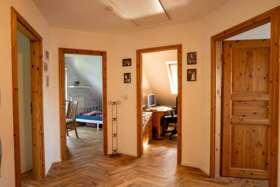 Flur mit Parkett, drei geöffnete Holztüren zu Wohnräumen, warmes Licht