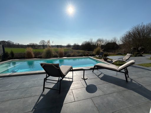 Pool mit Liegen, sonnigem Himmel und grünem Landschaftshorizont im Hintergrund.