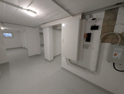 Heller Keller mit weißen Wänden, grauem Boden und wenigen Stromanschlüssen.