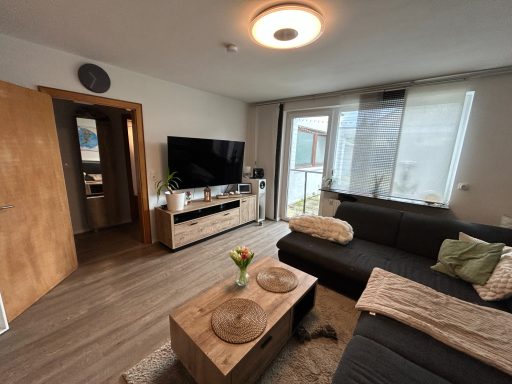 Heller Wohnraum mit Sofa, Couchtisch, TV und Zugang zu einem Balkon.