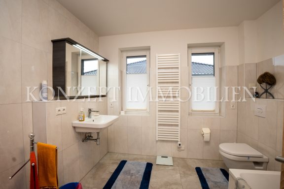 Helles Badezimmer mit Waschbecken, WC und Fenster, zeitgemäße Fliesen und Handtuchhalter.