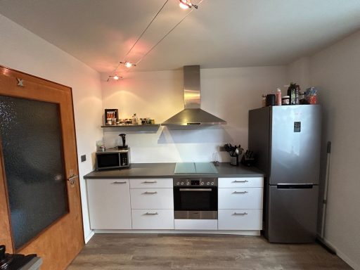 Moderne Küche mit Kochfeld, Dunstabzug, Kühlschrank und hellem Holzfußboden.