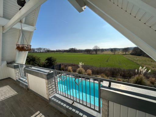 Blick auf eine grüne Wiese und Pool von einem Balkon aus unter klarem Himmel.