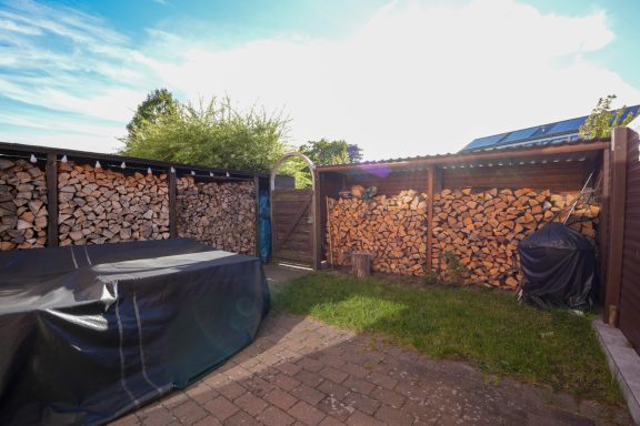 Brennholz für den Winter, ordentlich gestapelt hinter einem Gartenzaun.