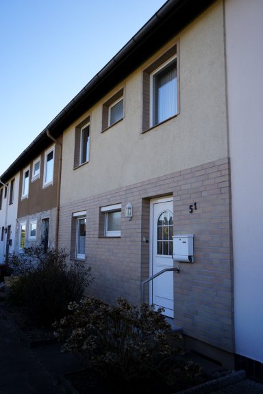 Einfamilienhaus mit Eingangstür und Fenstern, moderne Fassade in neutralen Farbtönen.