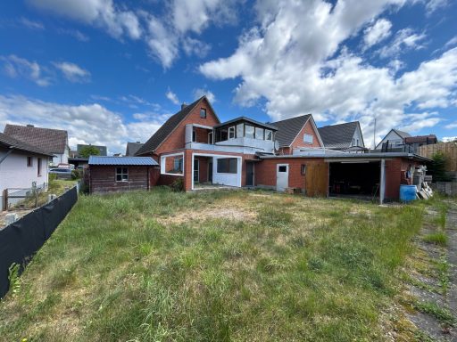 Rotes zweigeschossiges Haus mit Wiese und Wolken am Himmel im Hintergrund.