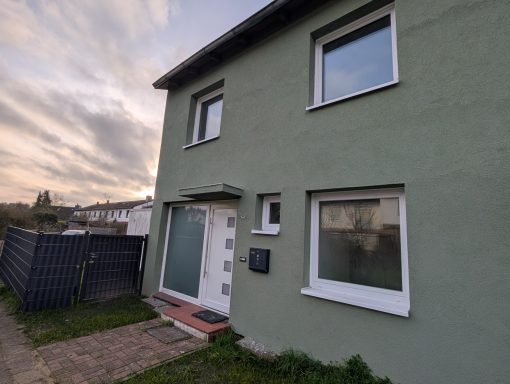 Zweistöckiges, grünes Wohnhaus mit einem Eingang und großen Fenstern.