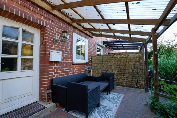 Gemütliche Terrasse mit schwarz-weißen Möbeln und Sichtschutz aus Schilfrohr.