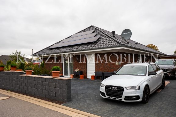 Modernes Haus mit Solarplatten, Satellitenschüssel und einem weißen Auto im Vordergrund.