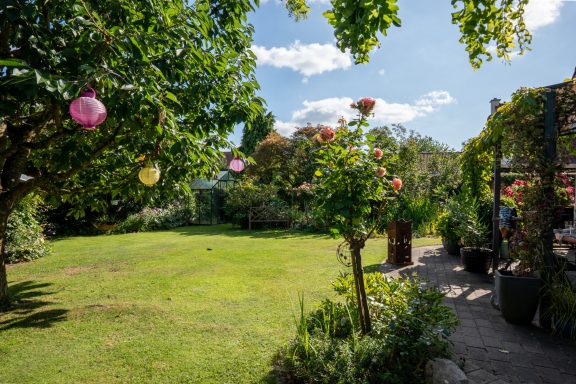 Garten mit Rasen, blühenden Büschen, Bäumen und Steinweg zu einer Terrasse