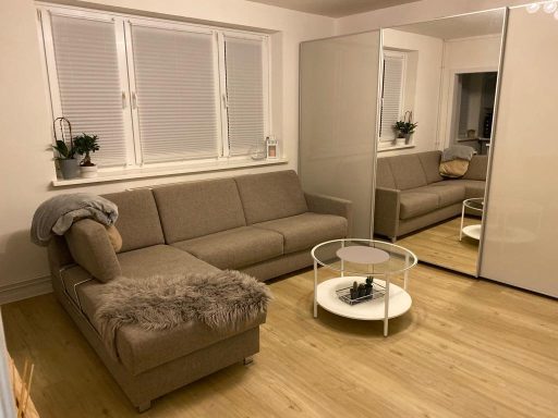 Helle Wohnzimmereinrichtung mit beigem Sofa, Couchtisch und großen Spiegeln.