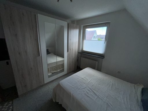 Helles Schlafzimmer mit einem Bett, Kleiderschrank und Fenster.