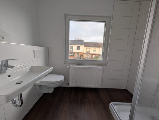 Helles Badezimmer mit WC, Waschbecken, Dusche und Fenster zur Außenansicht.