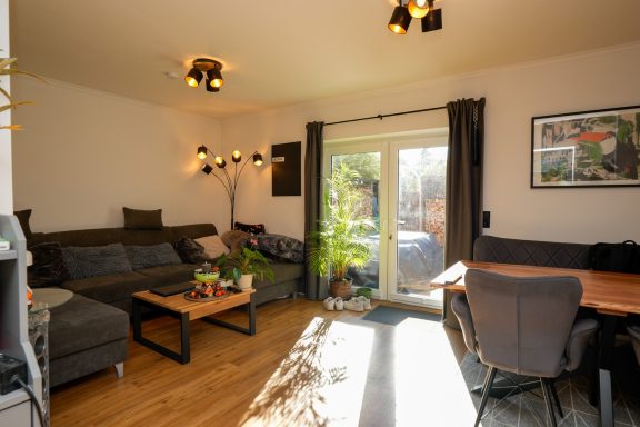 Heller Wohnraum mit Sofa, Tisch und Zugang zu einer Terrasse mit Pflanzen.