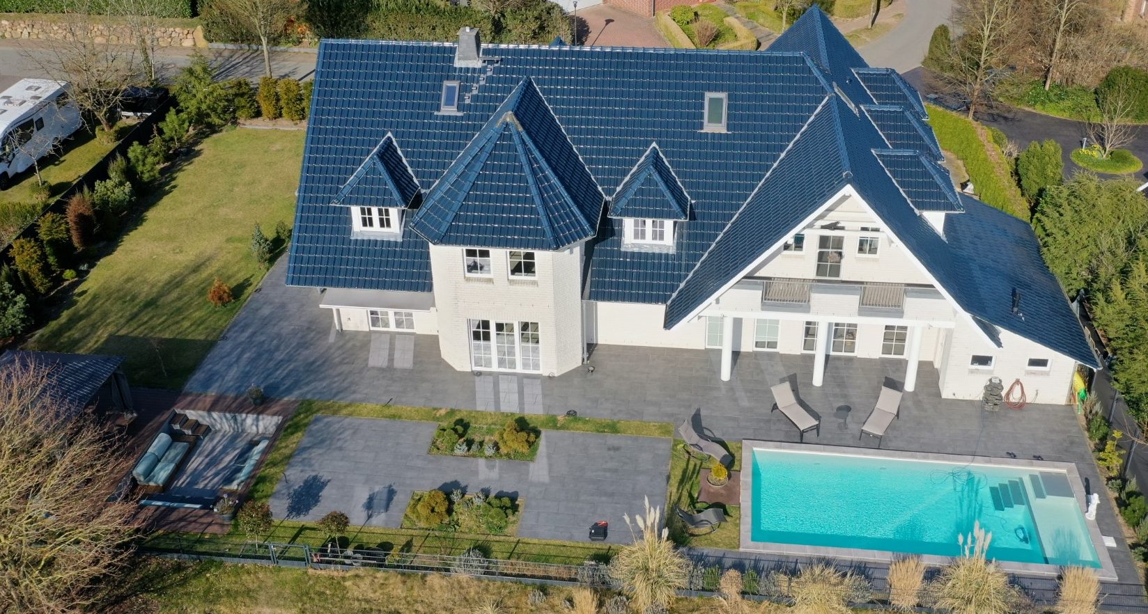 Elegantes Haus mit blauem Dach, großer Terrasse und Pool im Garten.