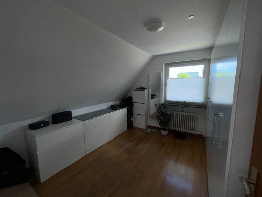 Heller Raum mit schrägem Dach, Fenster, weißen Möbeln und Holzfußboden.