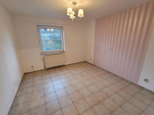 Helle, leere Zimmeransicht mit Fliesenboden und einem Fenster. Rosa Akzentwand vorhanden.