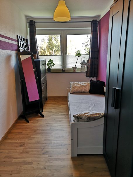 Helles Schlafzimmer mit Bett, Spiegel, Pflanzen und einem Schrank. Holzfußboden.